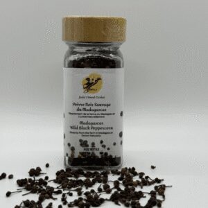 Glass jar of black peppercorns with scattered peppercorns around it.